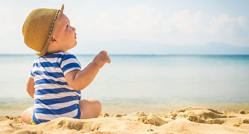 Bebé sentado en la arena de la playa con ropa cómoda de verano