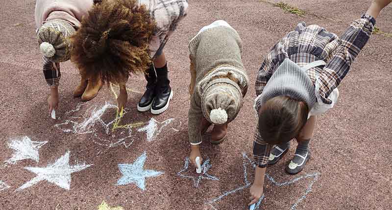 Niños pintando el suelo con tizas vestidos con las tendencias de otoño invierno 2022